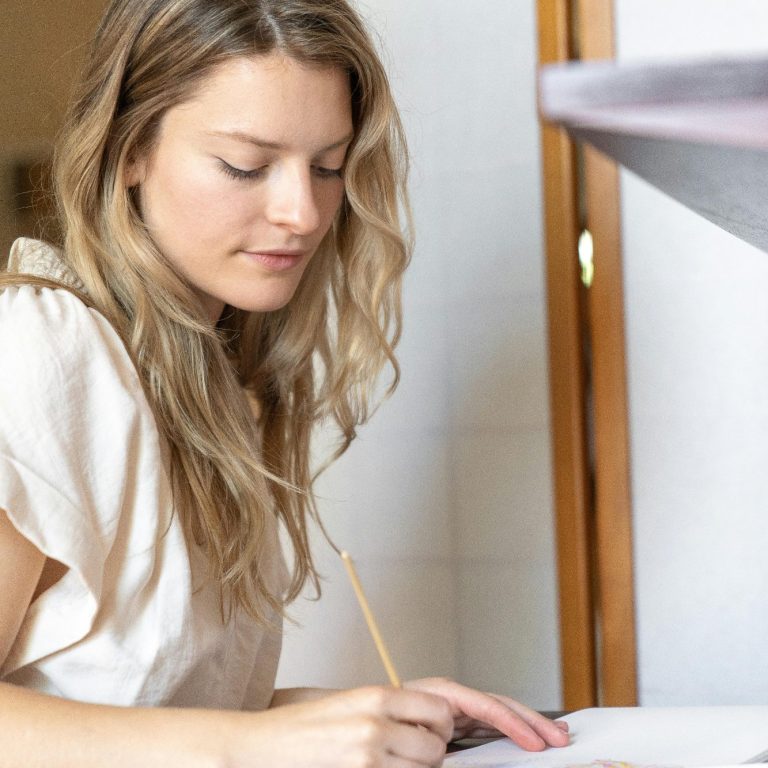 Executive function coaching for adults A woman with long, wavy hair writing on paper at a table.